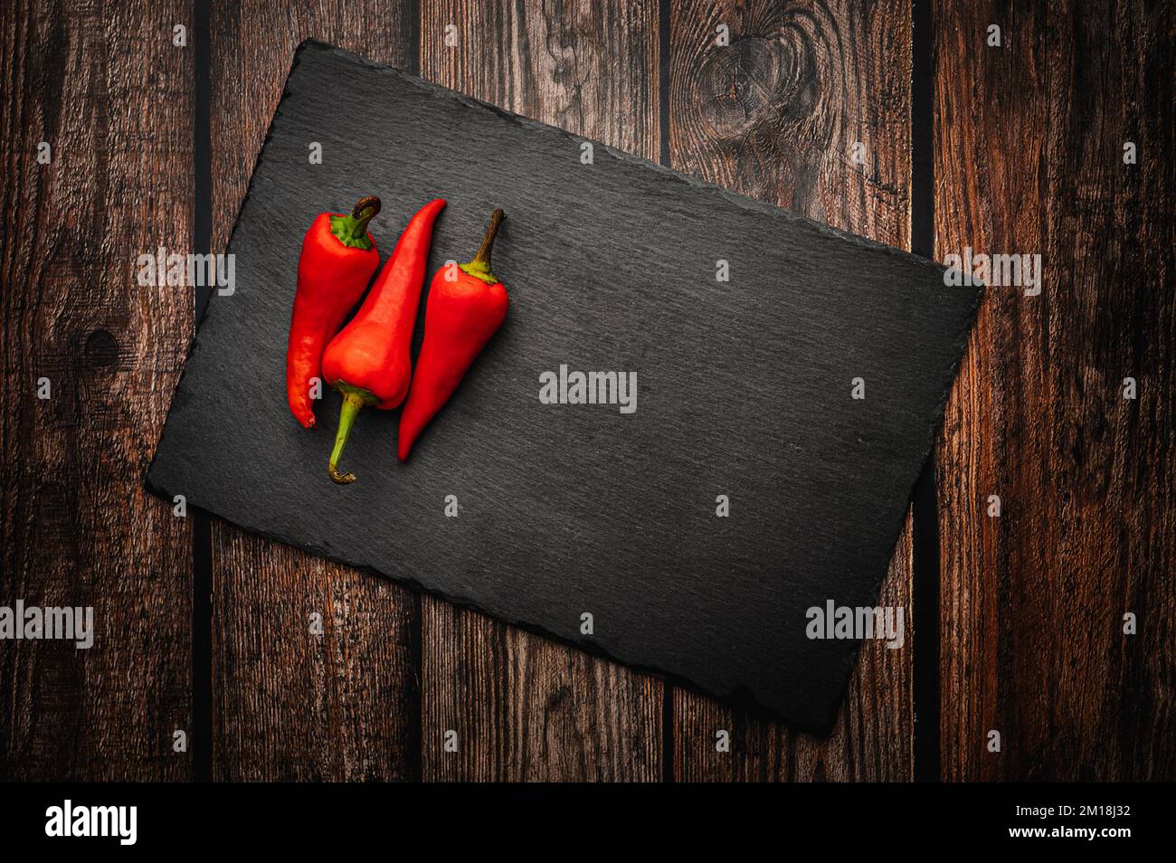 Red hot chili peppers on a slate board on a dark wooden table. Top down overhead view. Stock Photo