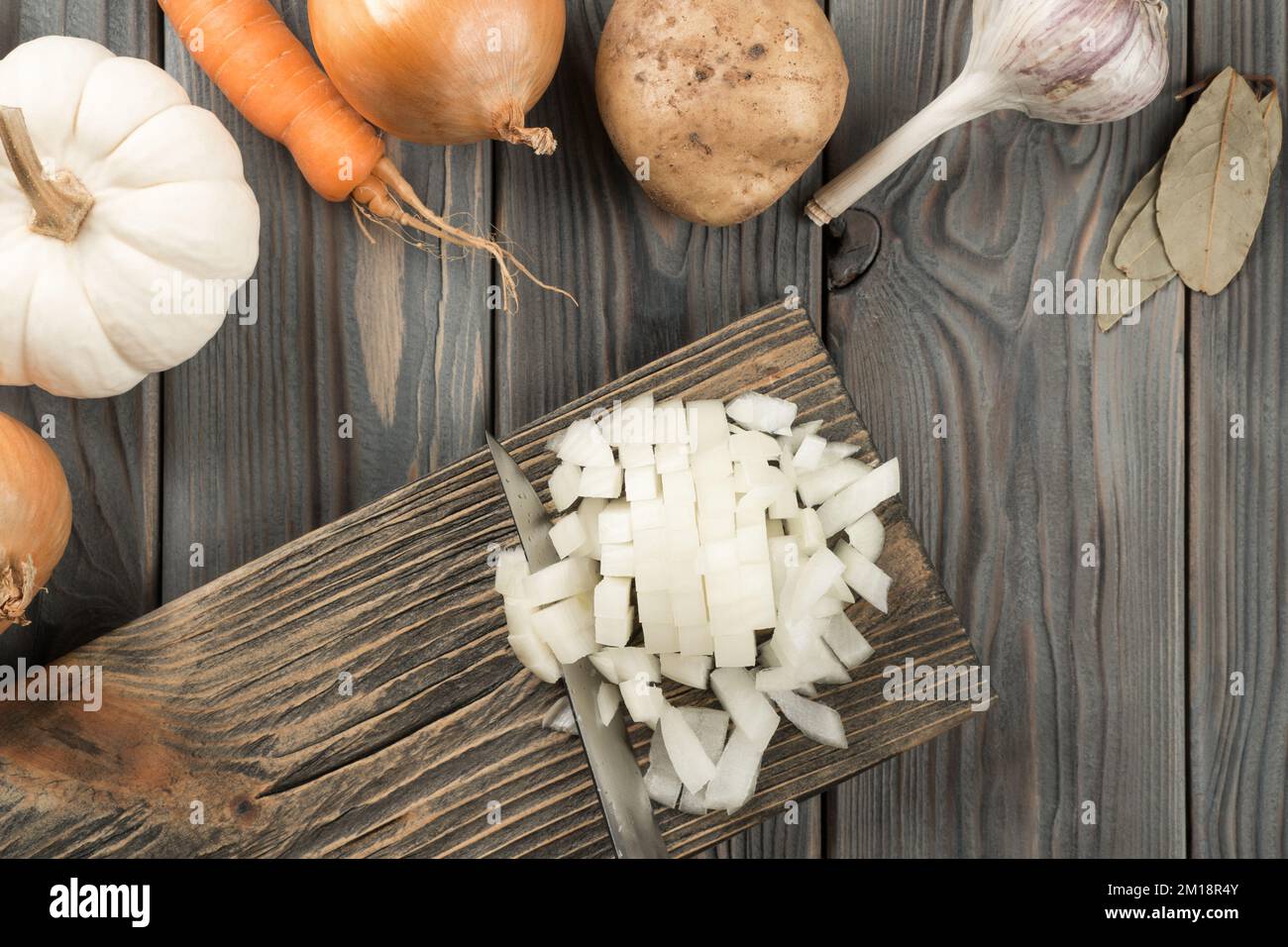 Cutting spicy onion with knife into cubes on kitchen wooden board. White diced onion. Flat lay