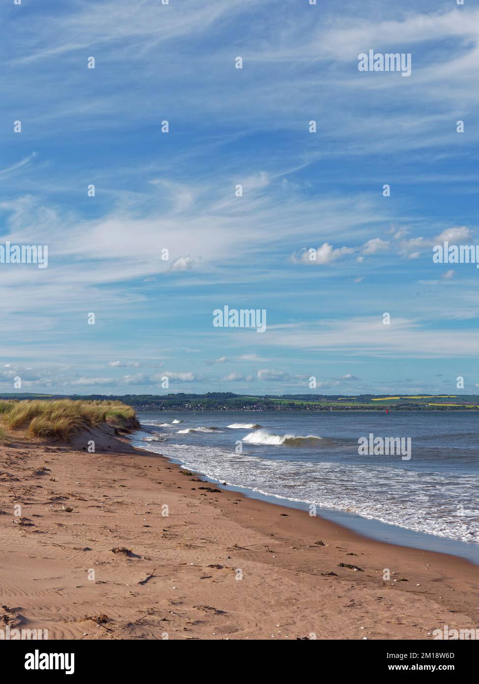 Waves coming in against the grass covered dunes of Tentsmuir point at the far point of the Estuary mouth. Stock Photo