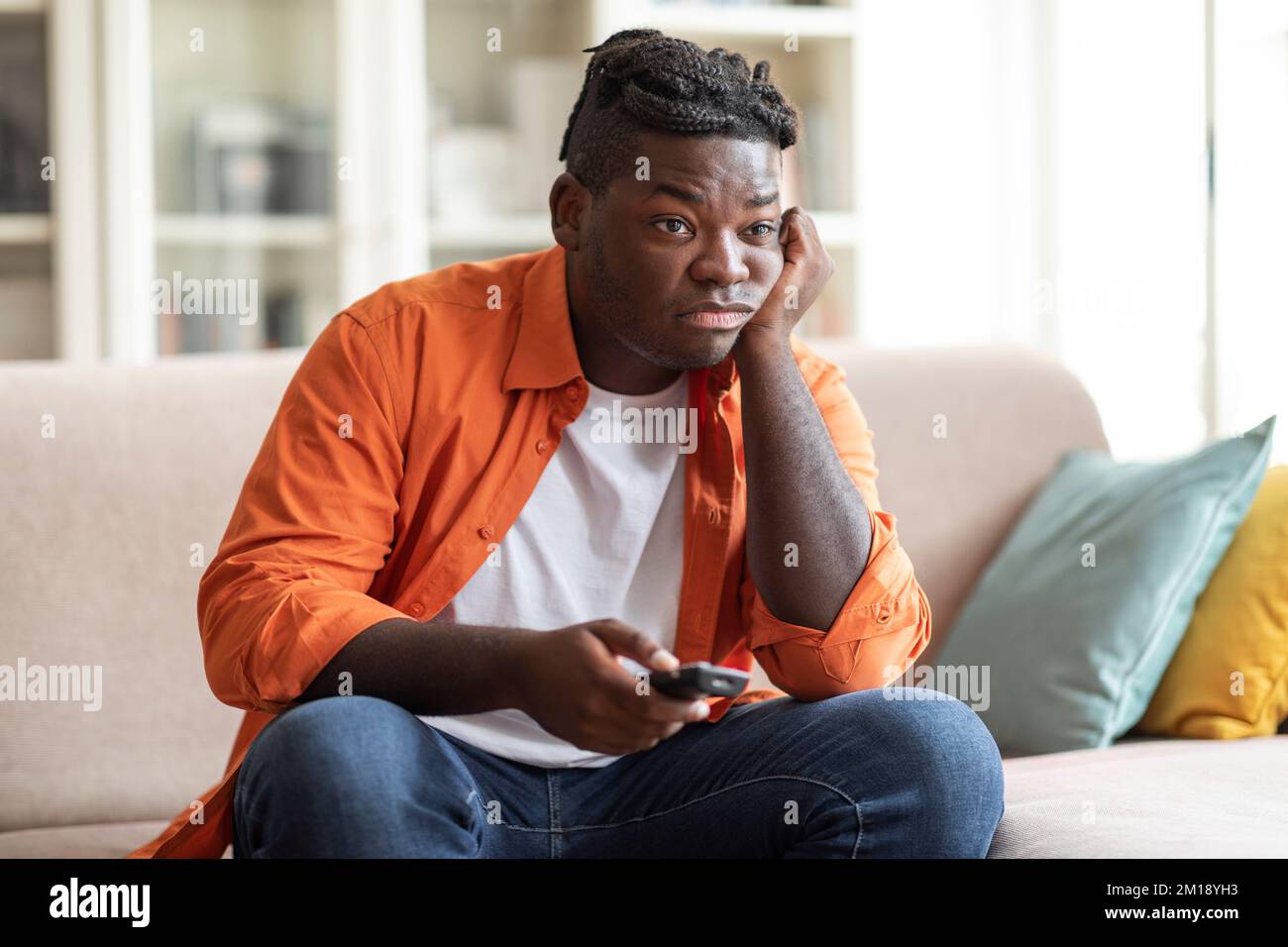 Boring african american guy sitting at home, switching tv Stock Photo