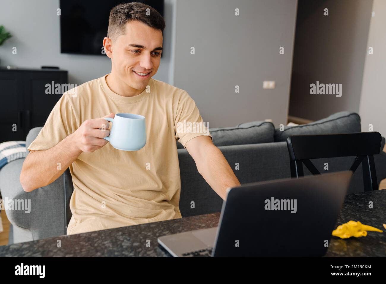 Young white man drinking tea and using laptop while sitting over table at home Stock Photo