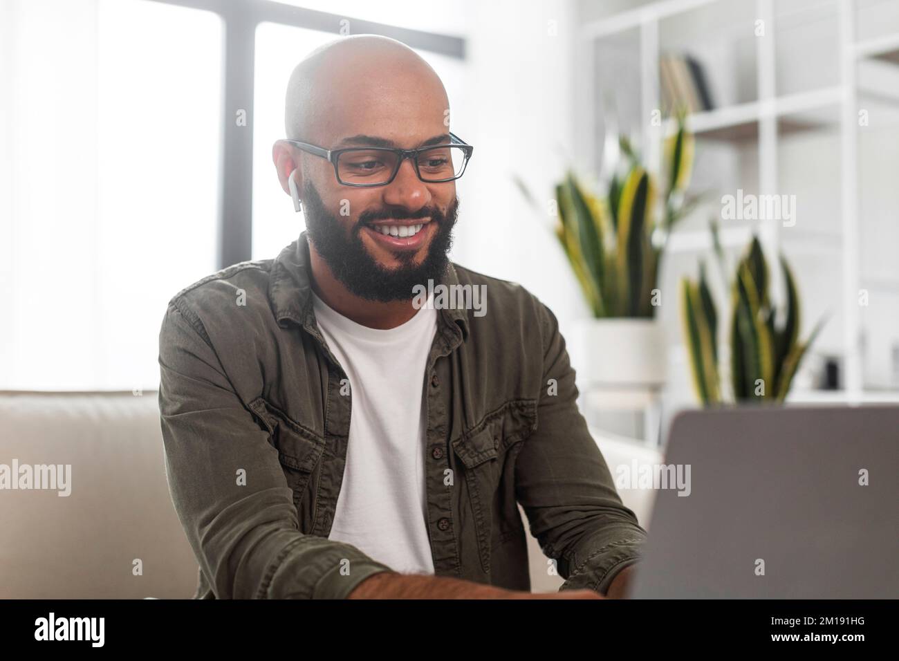 Happy latin businessman working on laptop computer, wearing earbuds and ...