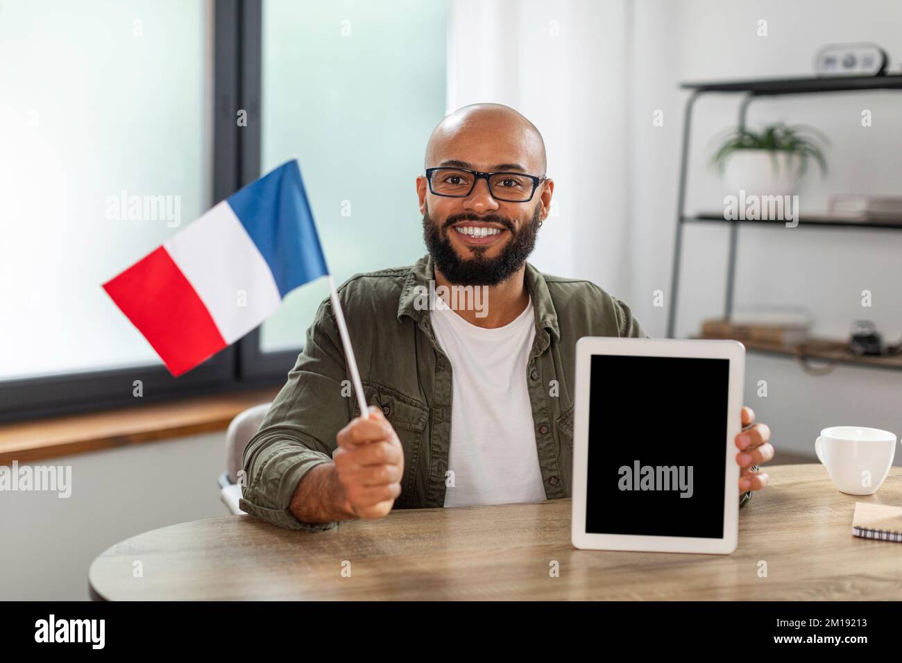 Happy latin man holding flag of France and showing tablet with blank