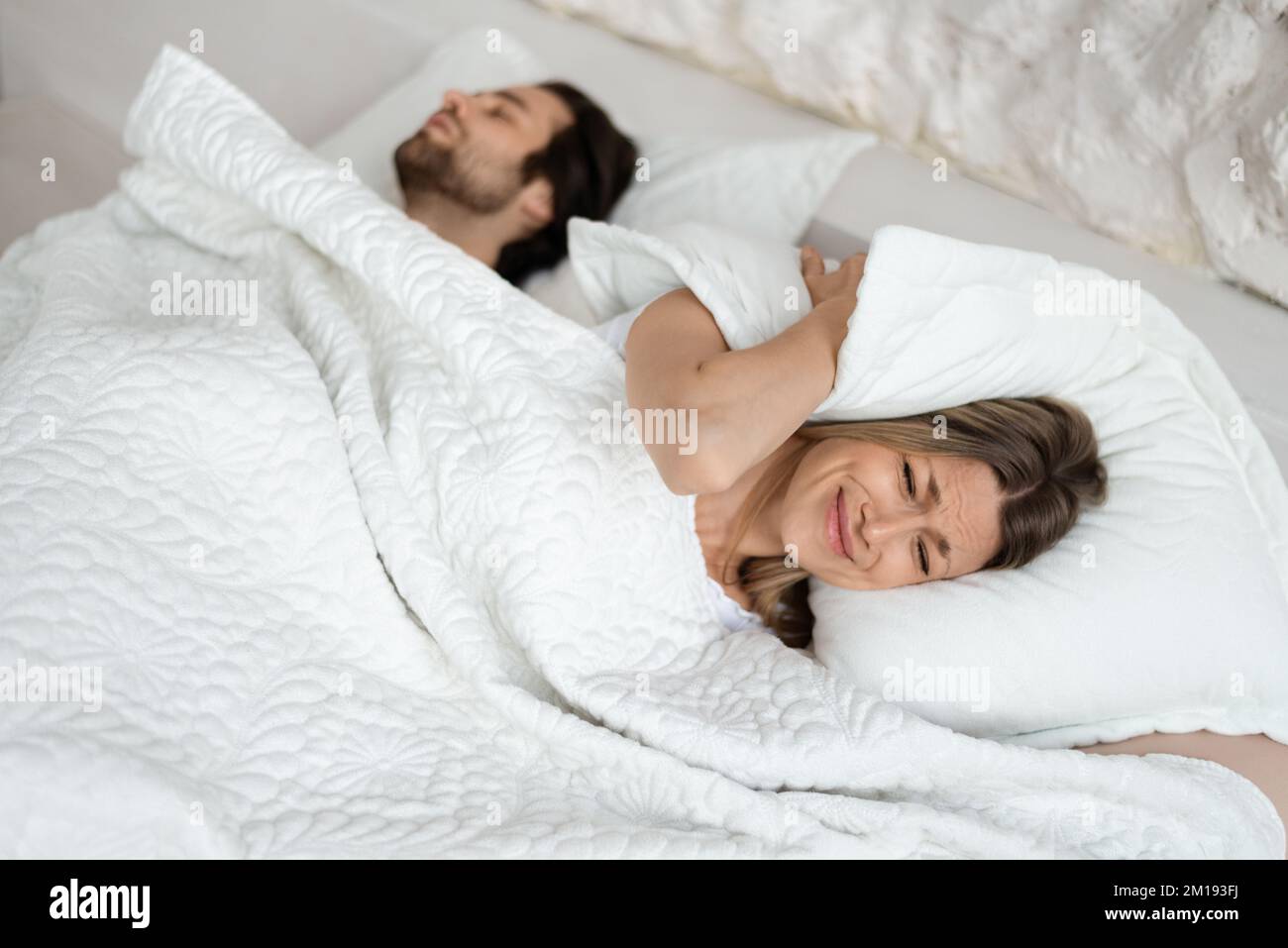 Angry woman covering ears with pillow, suffering noise while her