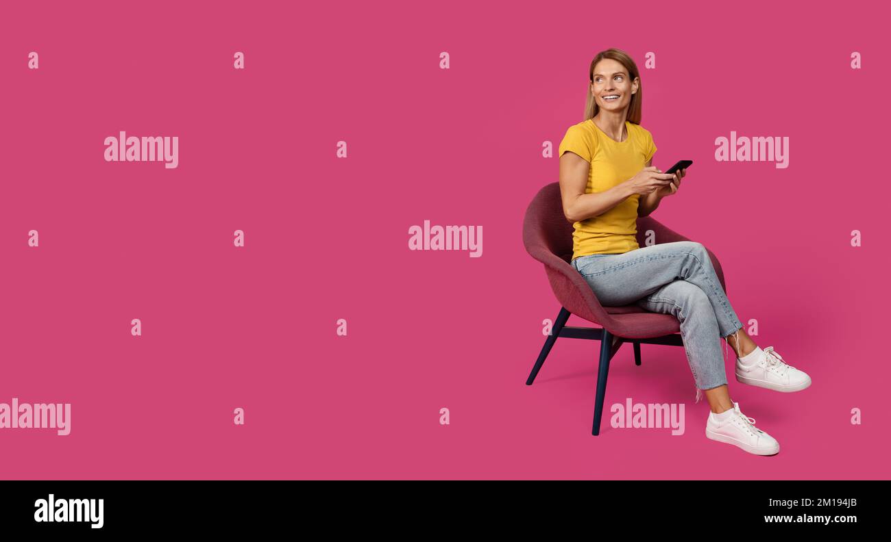 Cheerful adult caucasian female blonde in casual sitting on chair, chatting on smartphone Stock Photo