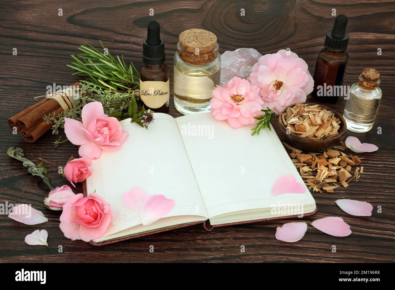 Aphrodisiac love potion preparation for Valentines Day. Magical spell recipe book or love letter with herbs, rose flowers, oil, spring water, crystal. Stock Photo