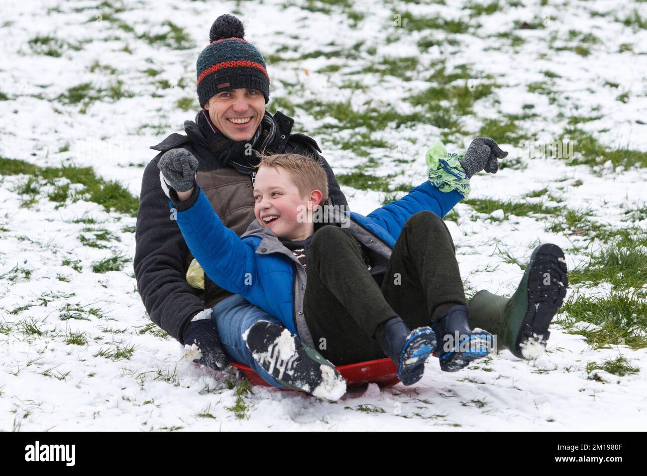 Chippenham, Wiltshire, UK, 11th Dec, 2022. As Chippenham residents wake up to their first snow of the year, a man and a child are pictured in a local park in Chippenham as they slide down a hill on a sledge. Credit: Lynchpics/Alamy Live News Stock Photo