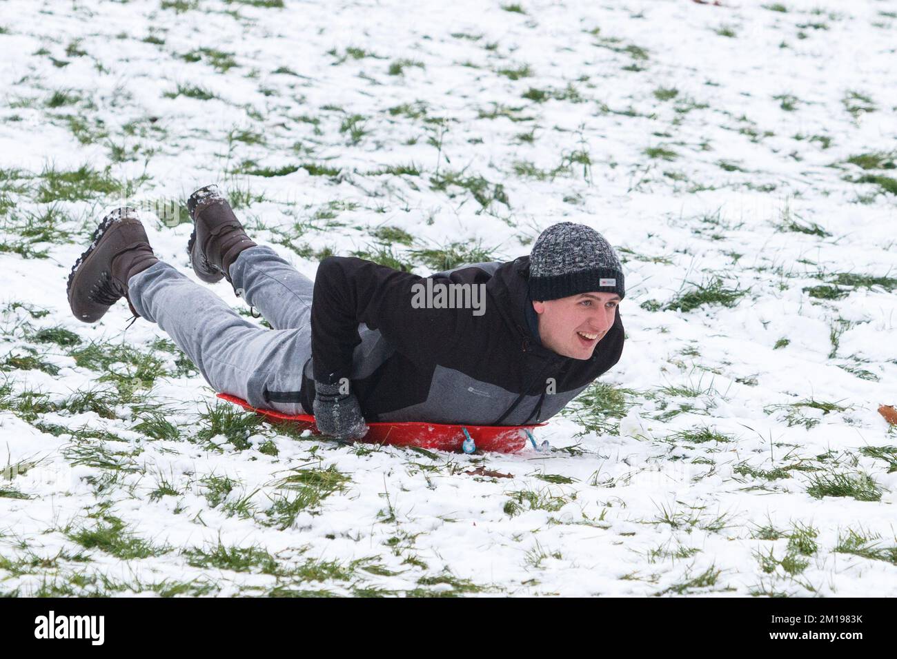 Chippenham, Wiltshire, UK, 11th Dec, 2022. As Chippenham residents wake up to their first snow of the year, a man is pictured in a local park in Chippenham as he speeds down a hill on a sledge. Credit: Lynchpics/Alamy Live News. Stock Photo