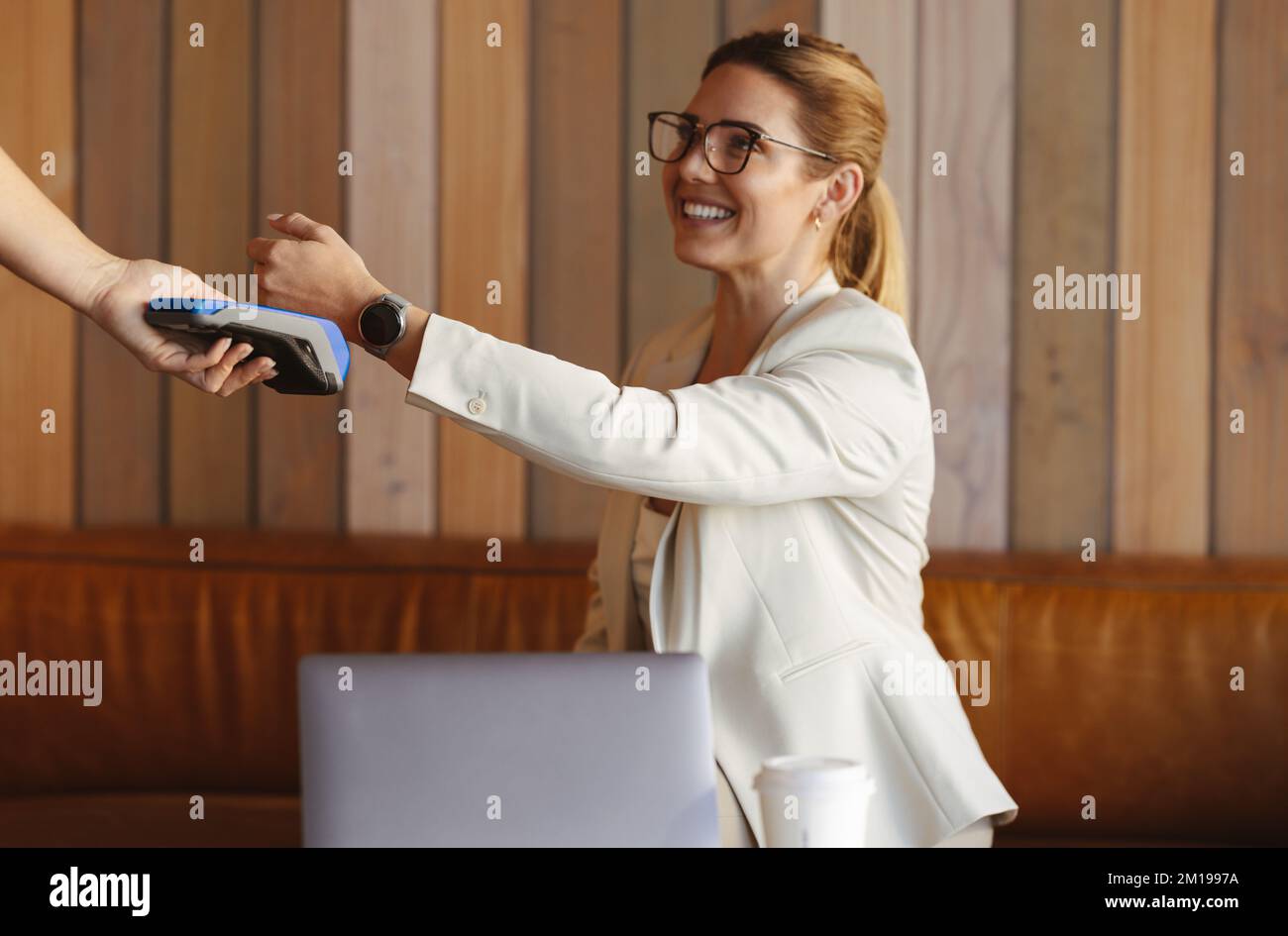 Woman scanning her smartwatch on a card machine to make a payment. Professional woman using NFC technology. business woman buying coffee while working Stock Photo