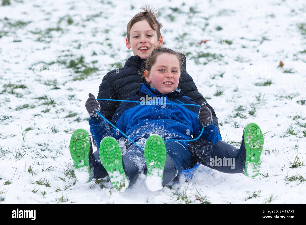 Chippenham, Wiltshire, UK, 11th Dec, 2022. As Chippenham residents wake up to their first snow of the year, two children are pictured in a local park in Chippenham as they speed down a hill on a sledge. Credit: Lynchpics/Alamy Live News. Stock Photo