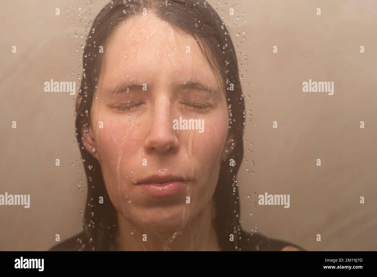 Young woman in shower with water running down her emotional face. Concept: feeling down, depression, domestic violence victim, had enough, depression Stock Photo