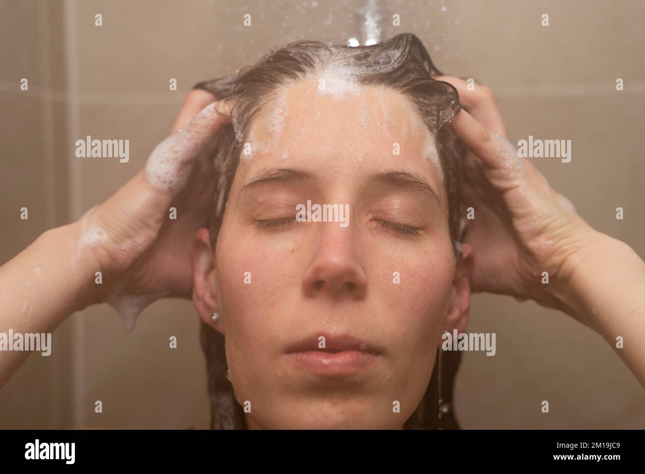 A Woman In Her Thirties Washing Her Hair In The Shower With Her Eyes Shut And Rubbing Shampoo