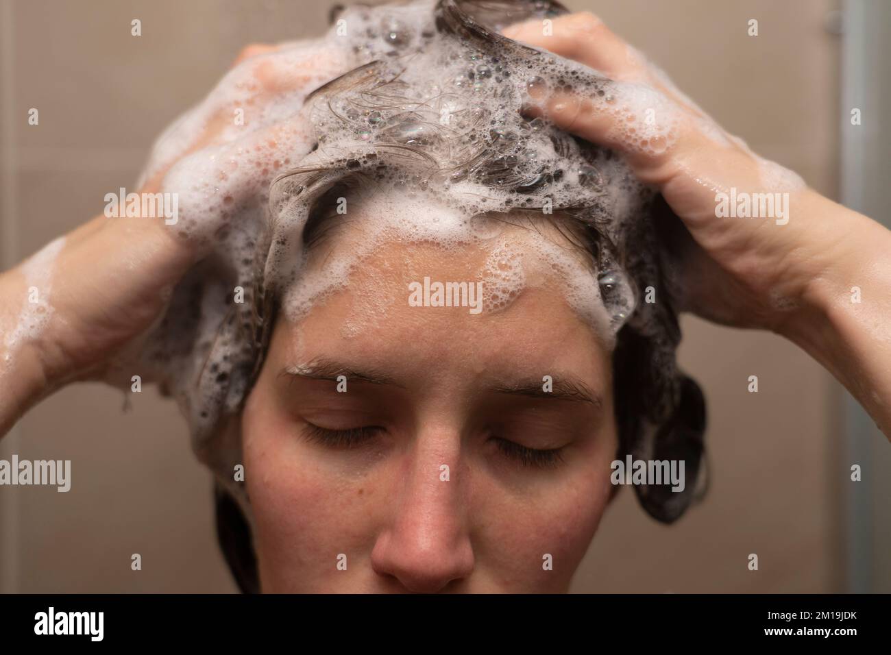 A woman in her thirties washing her hair in the shower with her eyes shut and rubbing shampoo suds into her hair Stock Photo