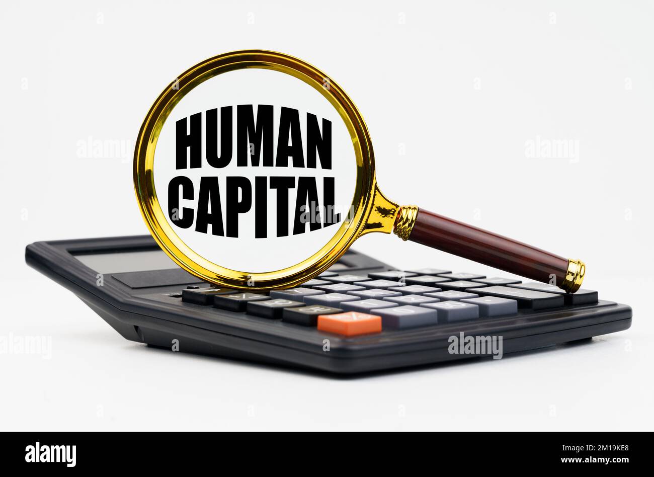 Finance and business concept. On a white background lies a calculator and a magnifying glass with the inscription - Human capital Stock Photo