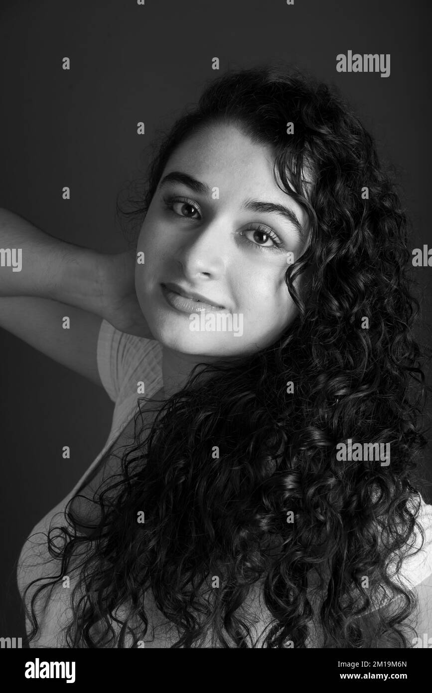 Black and white portrait of young beautiful woman with hand behind her neck. Looking at the camera. Against gray background. Stock Photo