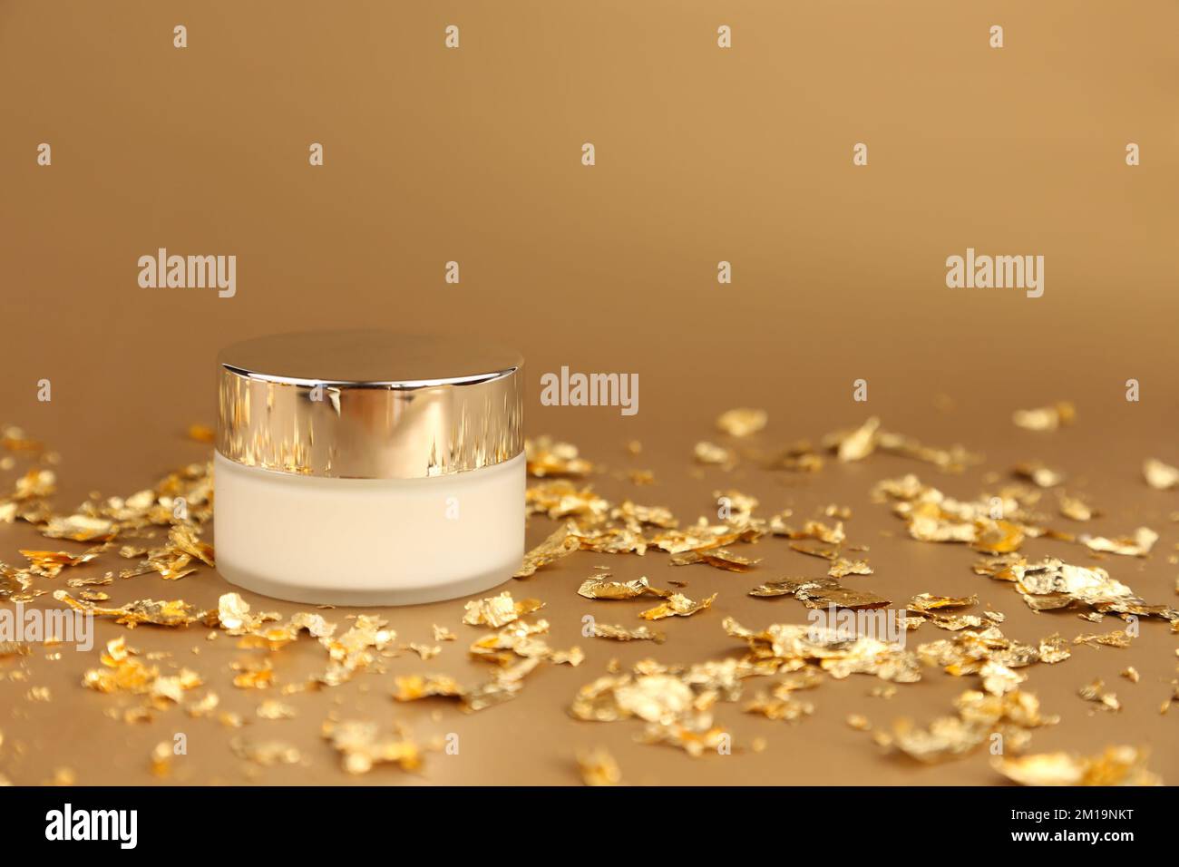 Cosmetic glass jar with white moisturizer. Luxurious anti-aging day cream with isoflavones and active microparticles of gold and pieces of gold paper Stock Photo