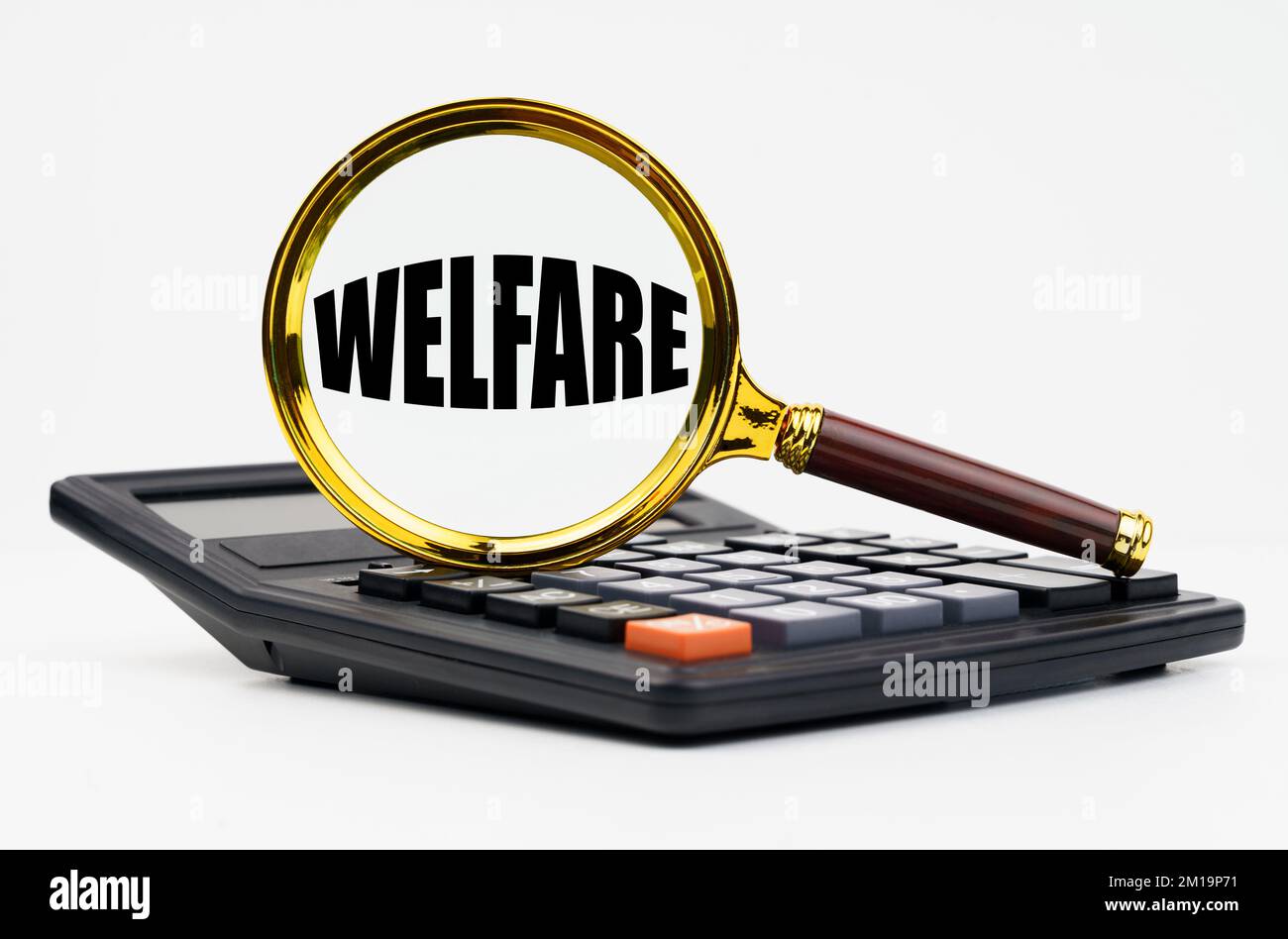 Finance and business concept. On a white background lies a calculator and a magnifying glass with the inscription - WELFARE Stock Photo