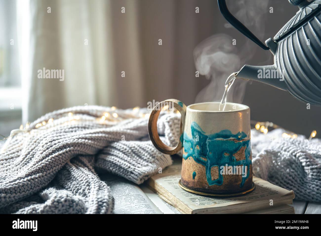 Beautiful handmade ceramic cup on a blurred background with a knitted element. Stock Photo