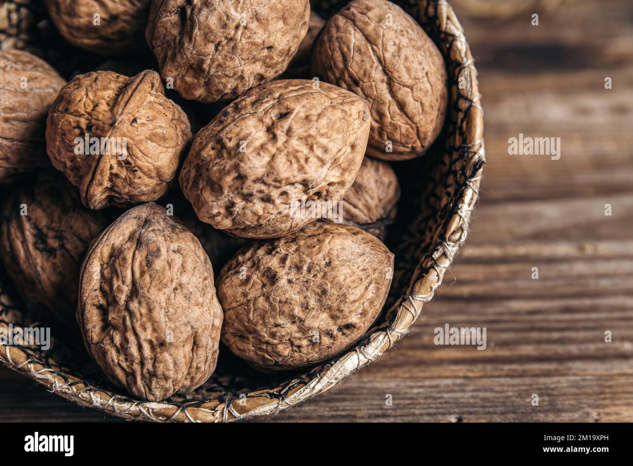 Close-up, whole walnuts in a wicker bowl on a wooden background. Stock Photo