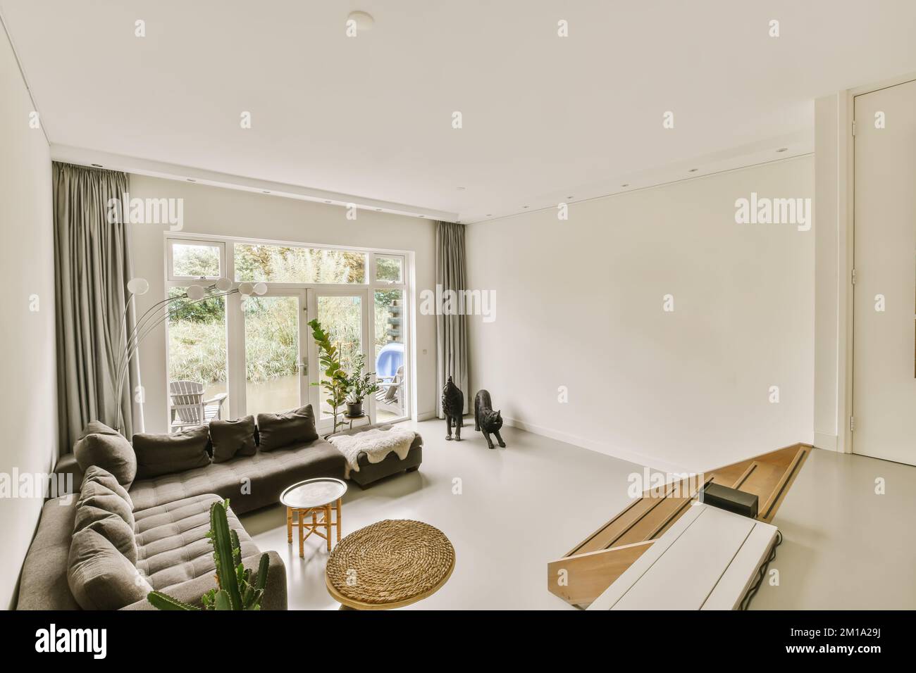 a living room with couches, coffee table and large window looking out onto the backyard garden in the background Stock Photo