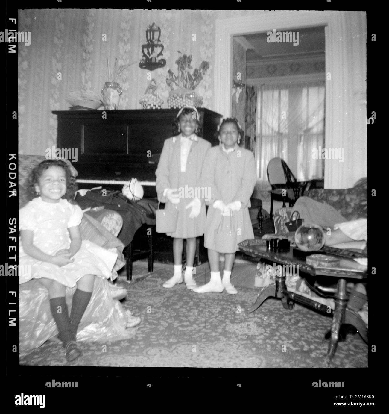 Two Girls Stand By Piano With Another Girl Seated In Chair Girls