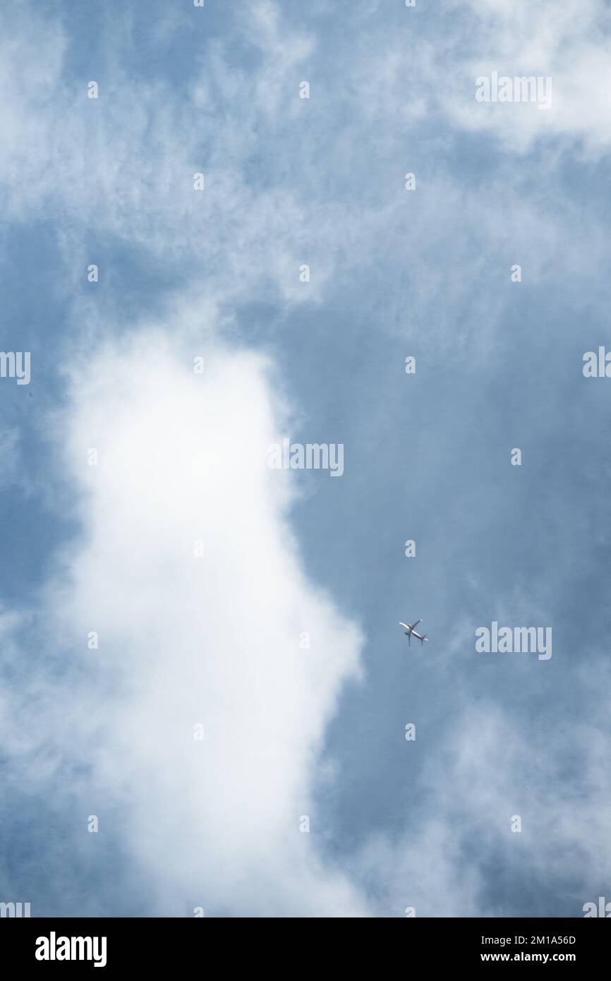 Distant airplane flying against a blue sky with hazy white clouds. Stock Photo