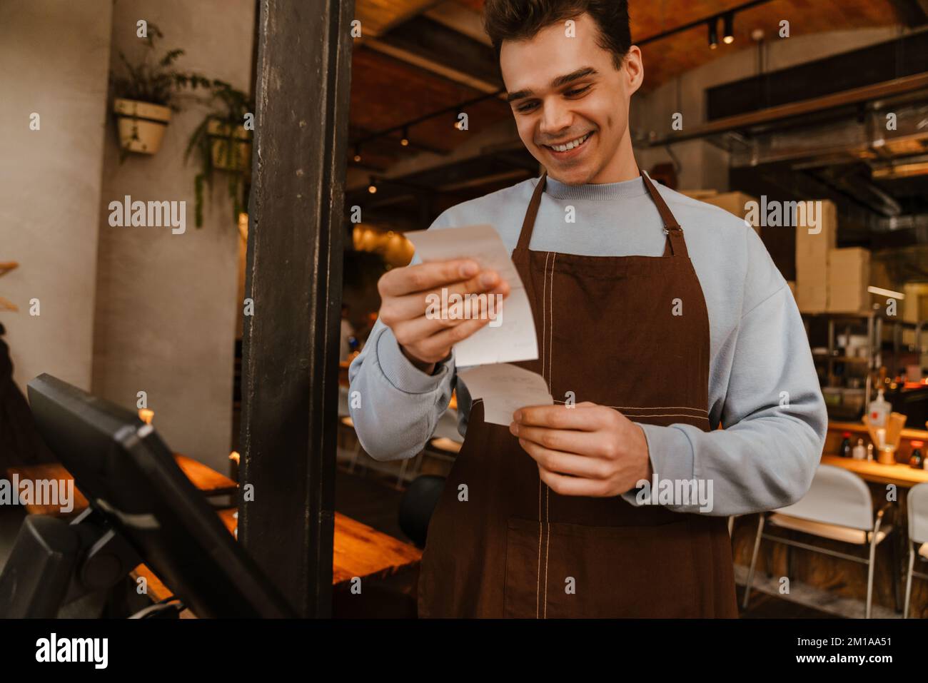 Young white waiter man wearing apron standing in front of computer and ...