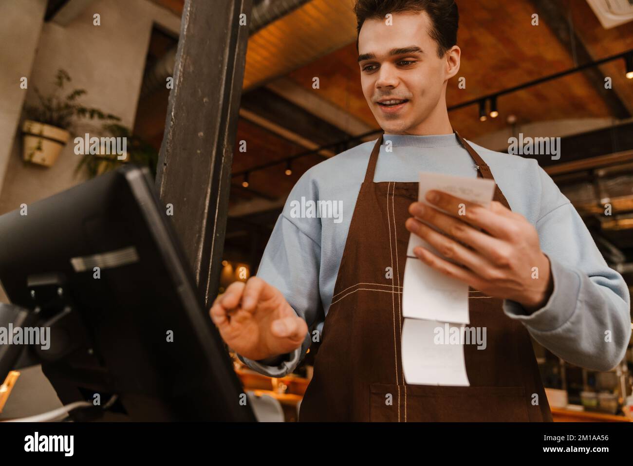 Young white waiter man wearing apron standing in front of computer and ...