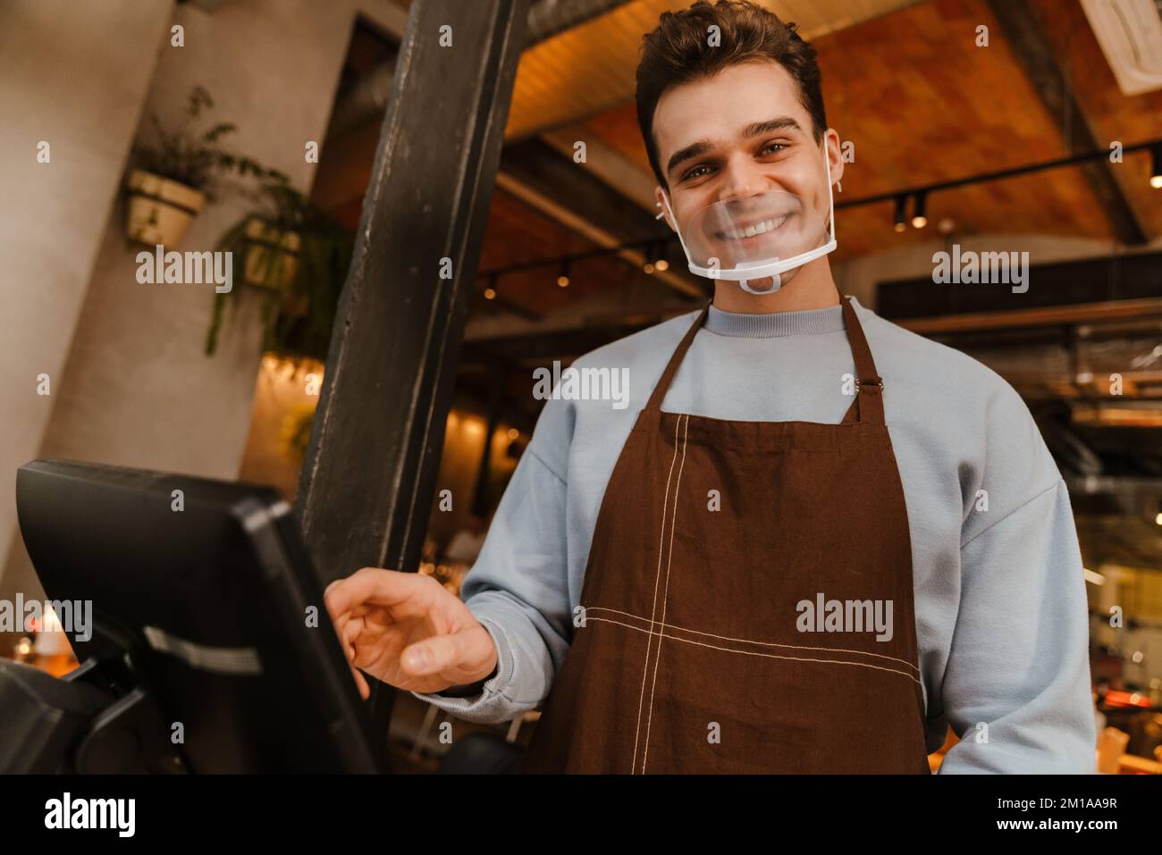 Young white waiter man wearing apron standing in front of computer and ...