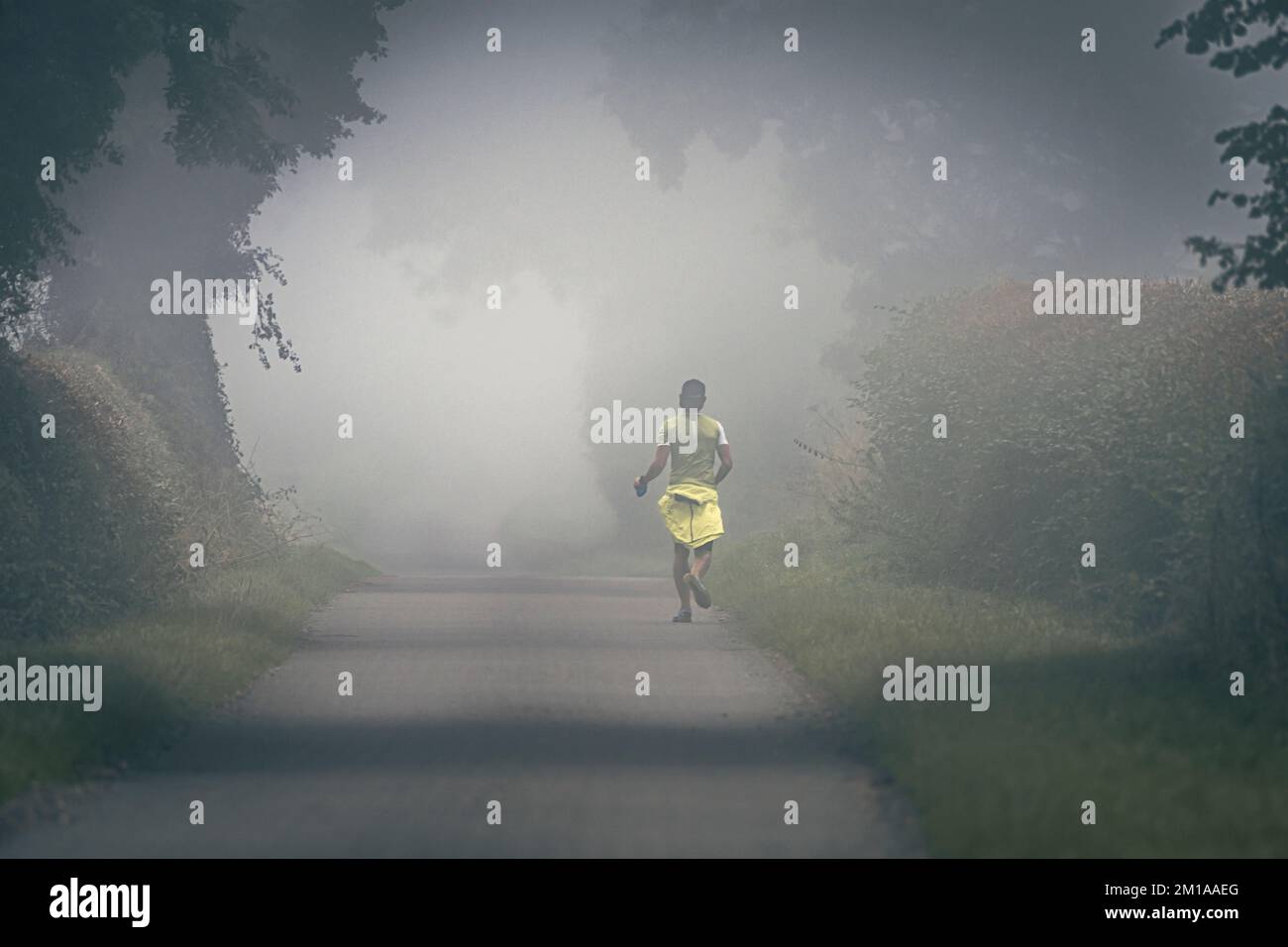A runner training on a very misty morning on a country lane. Stock Photo
