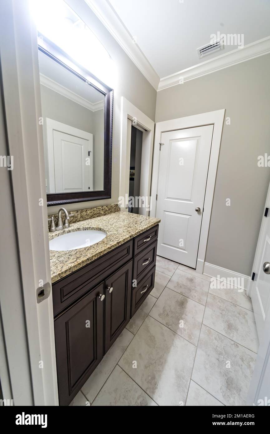 A modern new construction small guest bathroom with espresso cabinets, granite countertops, a tile floor and a mirror Stock Photo