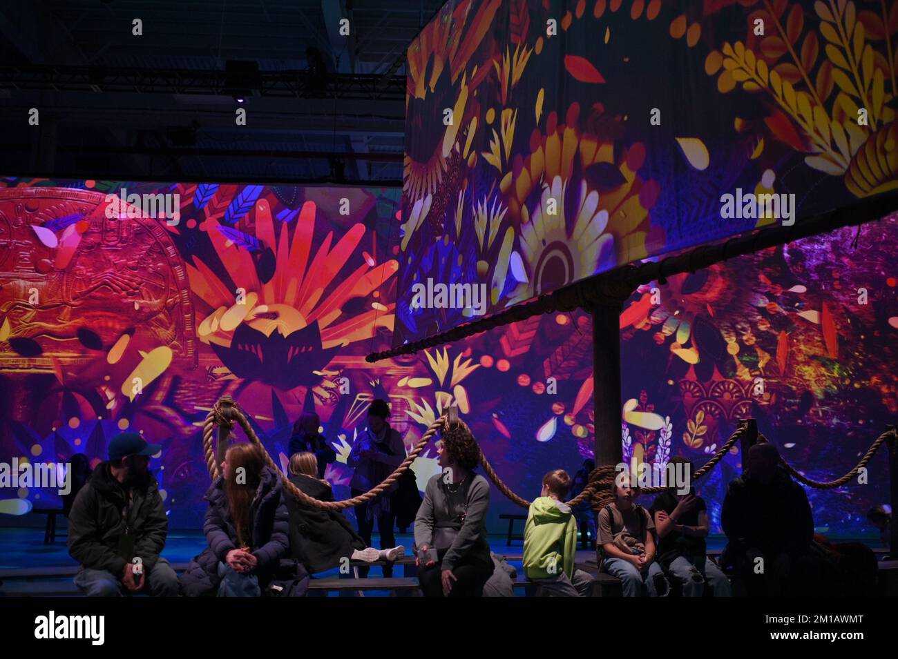 Visitors sit in a large room where a multimedia projection is presented ...