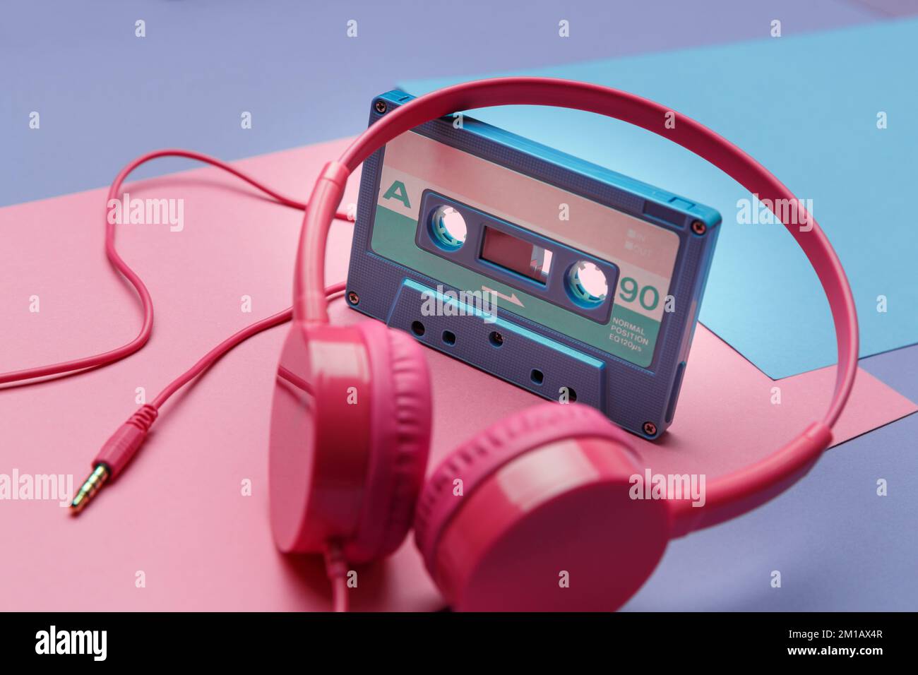 Pink headphones and blue tape audio cassette on a bright pink, violet