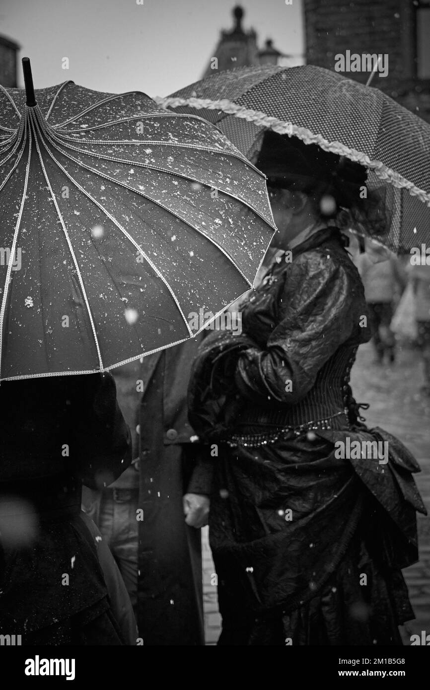 A group of women, dressing in Victorian clothes for a Steampunk event in Haworth, West Yorkshire, shelter from the snow under decorative umbrellas Stock Photo