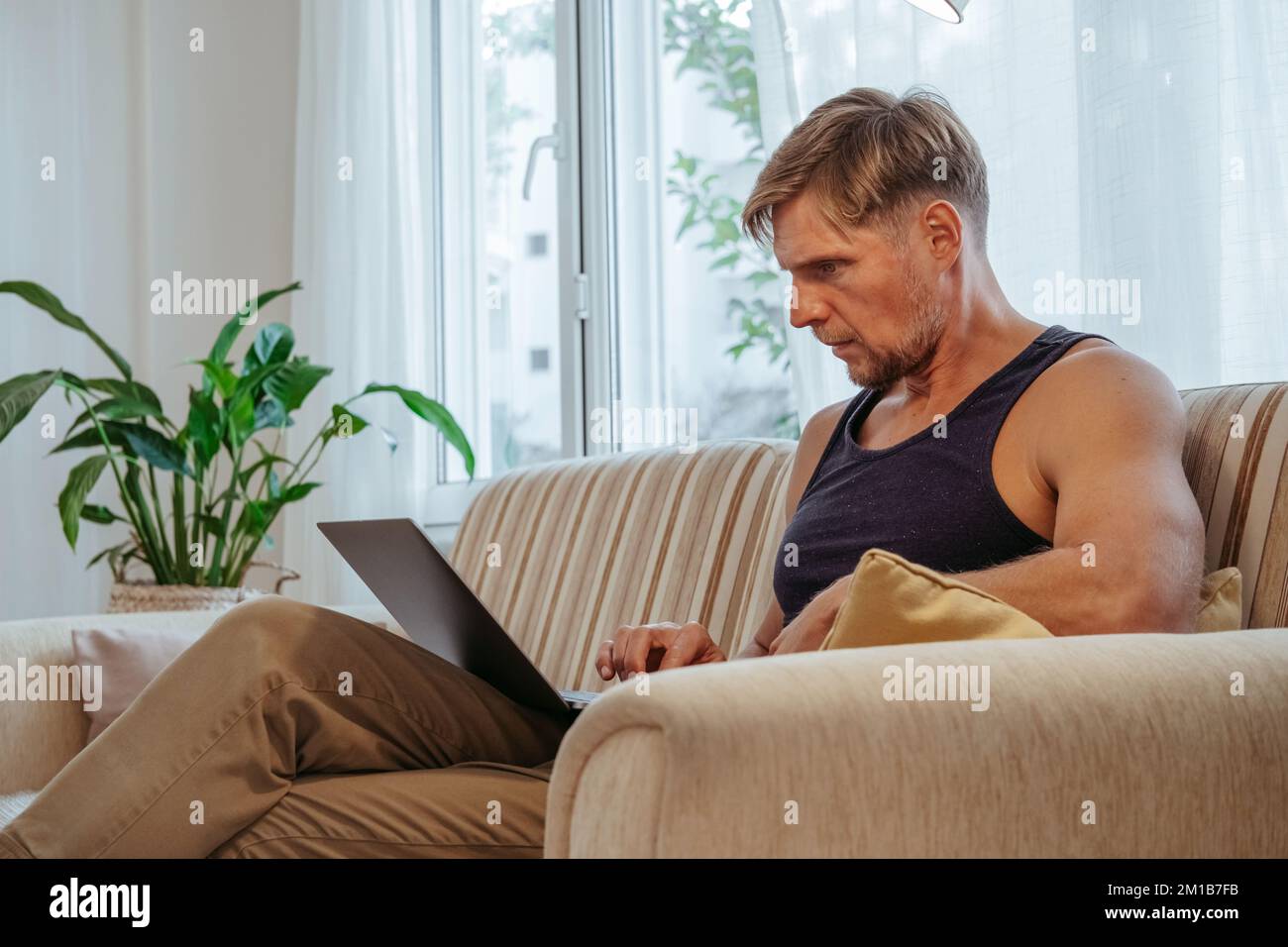 Man sitting on couch in living room with laptop. Handsome guy using