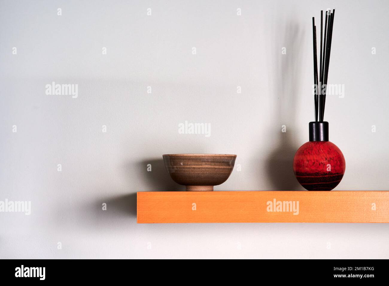 reed diffuser and small bowl on wooden shelf with shadows on wall Stock Photo