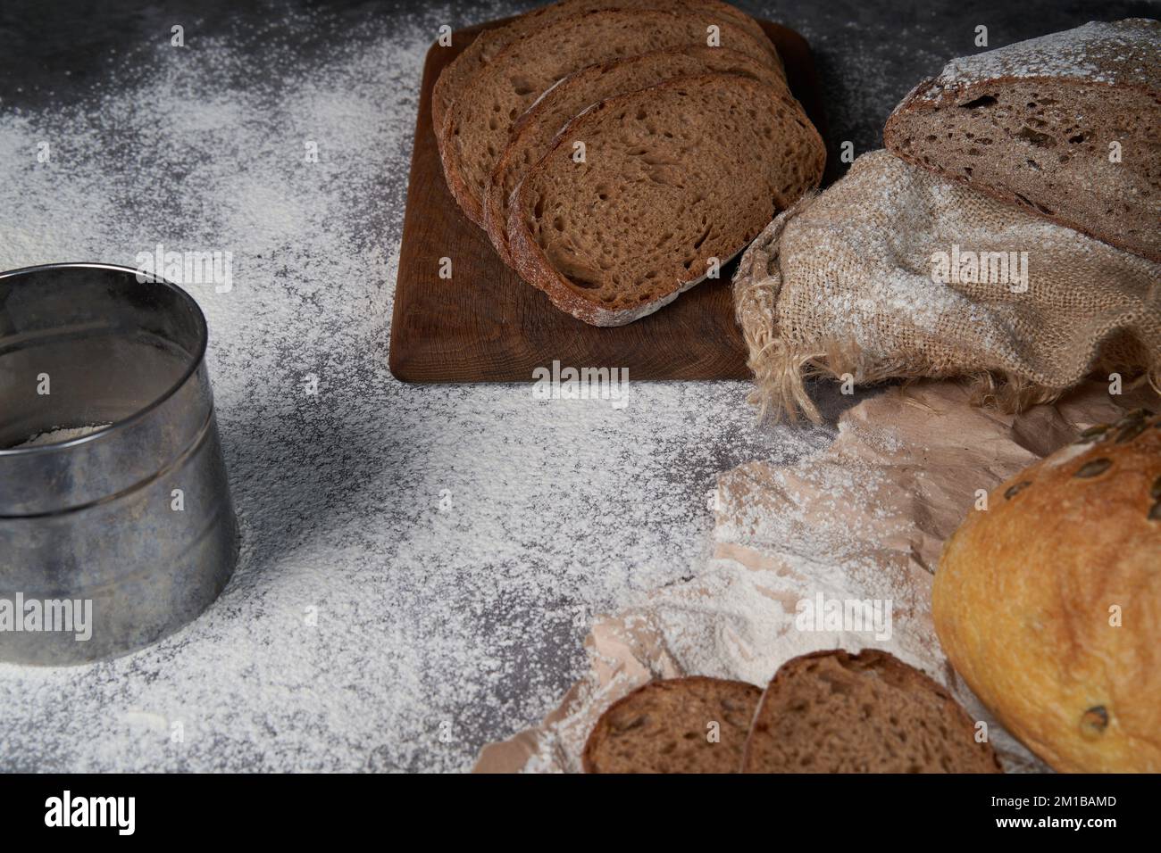Top view of various types of bread, sliced and whole, flour, crumpled paper and burlap on a wooden table. High angle. Stock Photo