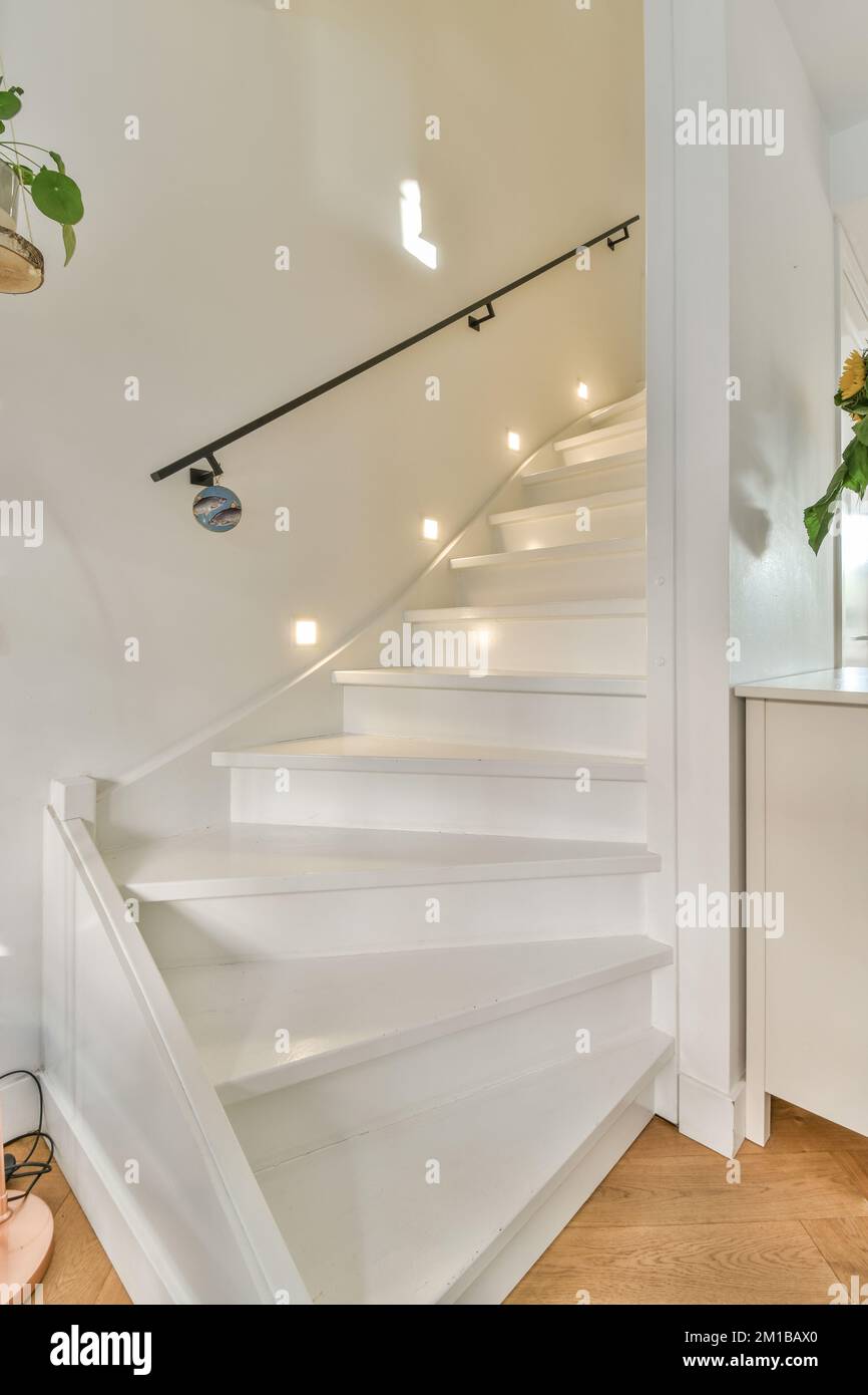 a white staircase in a house with wood floors and light fixtures on the wall behind it is an open door Stock Photo