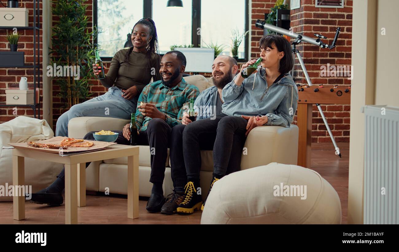Cheerful people clinking bottles of beer and watching movie on tv