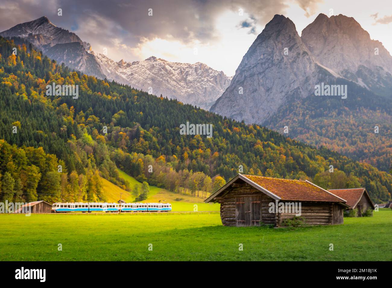 Train in Bavarian alps at autumn and wooden barns at sunset, Garmisch, Germany Stock Photo