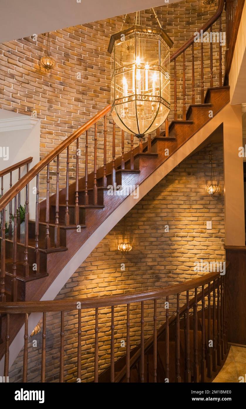 Lit chandelier above main wooden twisting staircase with curved