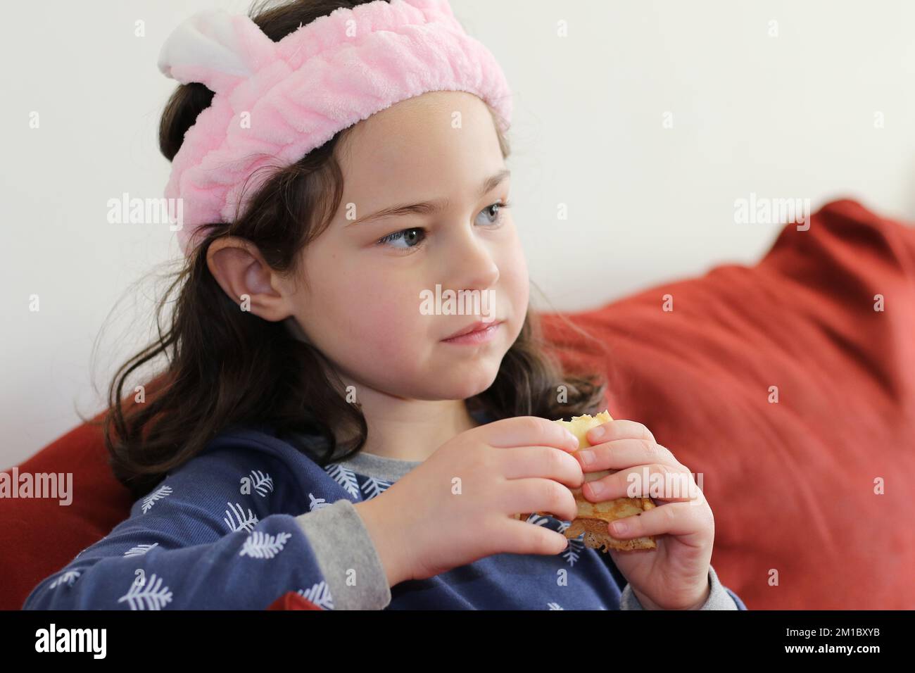 cute little girl in a pink head dress is eating crepes on the couch ...