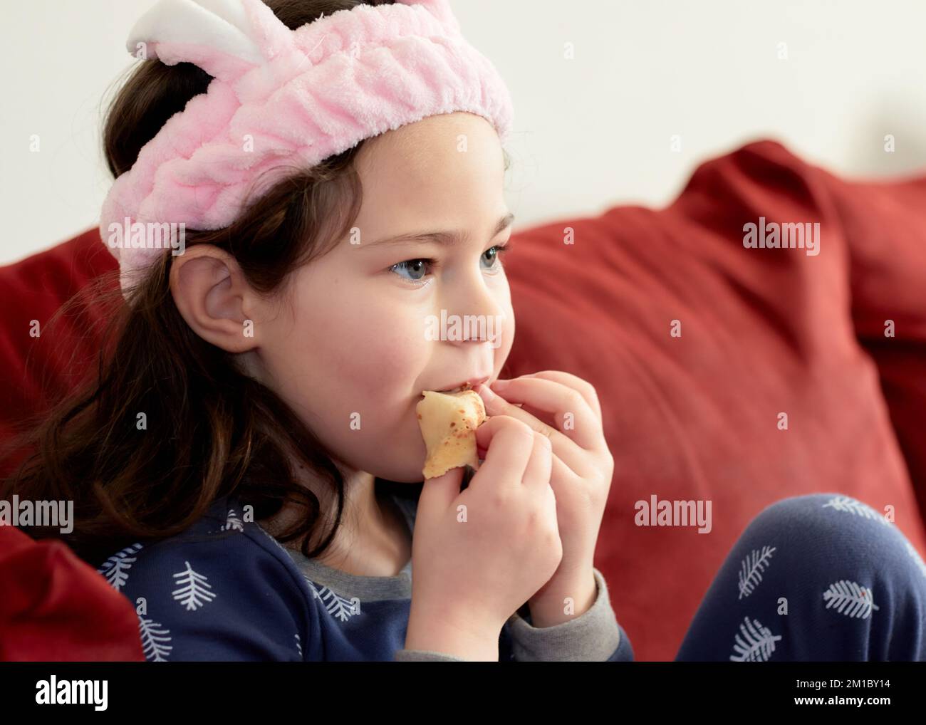 cute little girl in a pink head dress is eating crepes on the couch ...