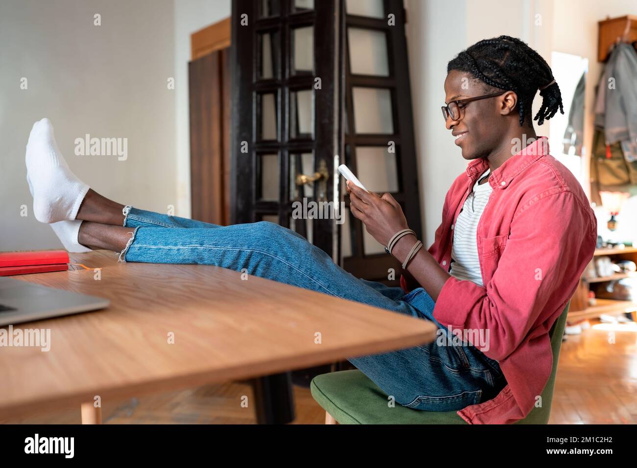 Smiling African guy freelancer using smartphone during working hours while working from home Stock Photo