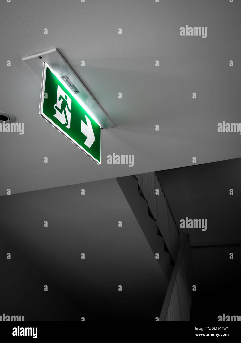 Fire exit sign. Green emergency exit sign hanging from white ceiling
