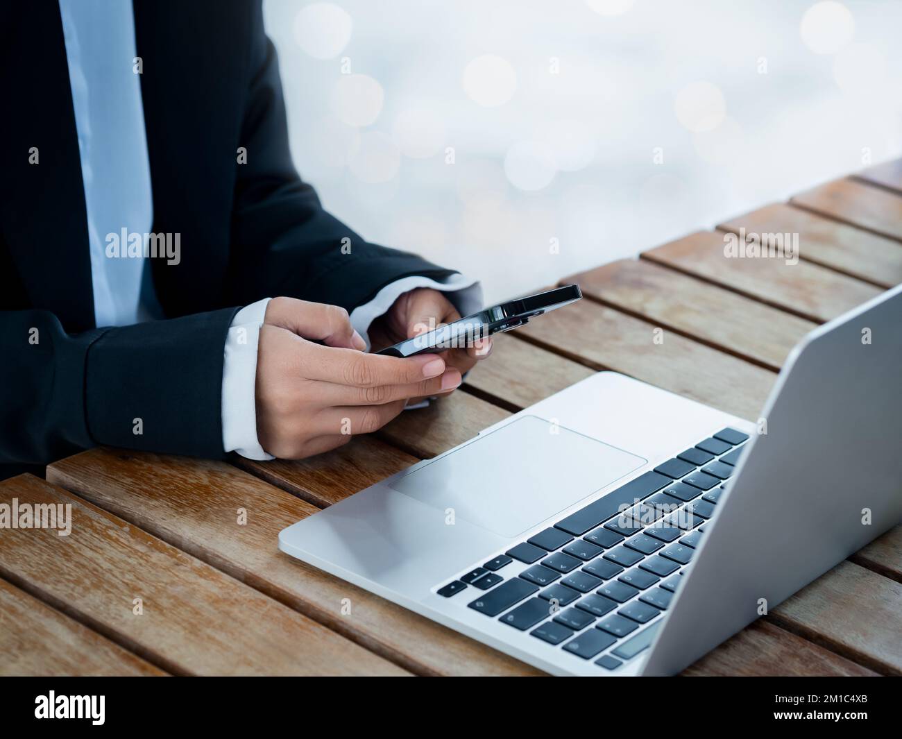 Black smart mobile phone in business woman's hand in suit who holding and using near the notebook computer on desk. Texting, cybersecurity, investment Stock Photo