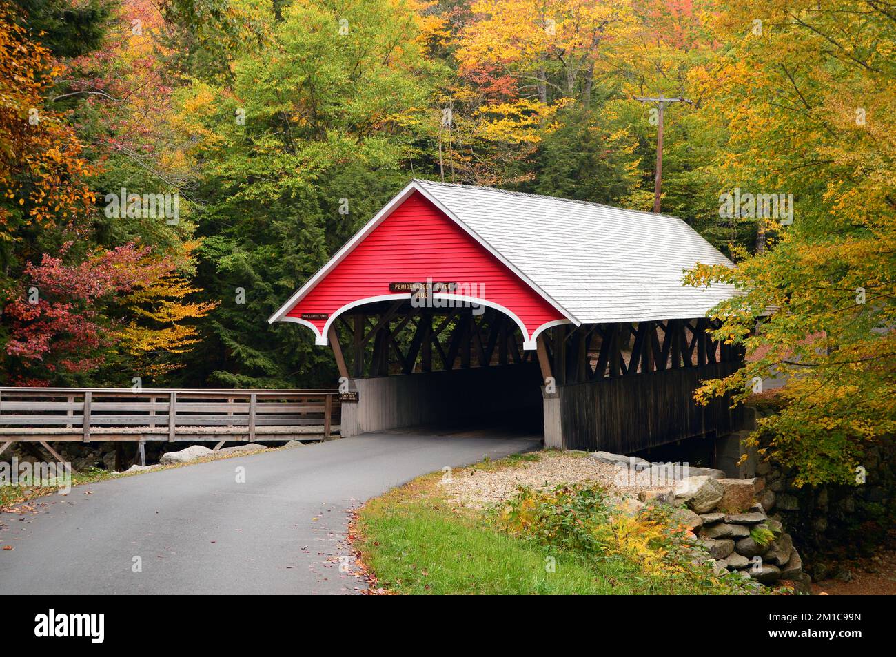 A quaint fall covered bridge is framed with autumn foliage and leaves  in New England Stock Photo