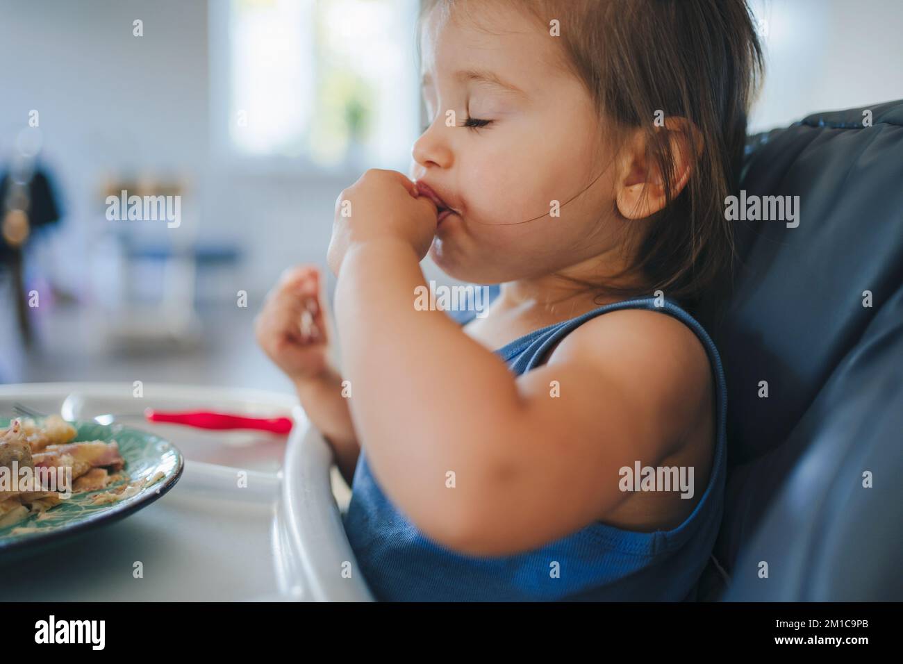 Baby girl self feeding by hands, taking with fingers food from plate