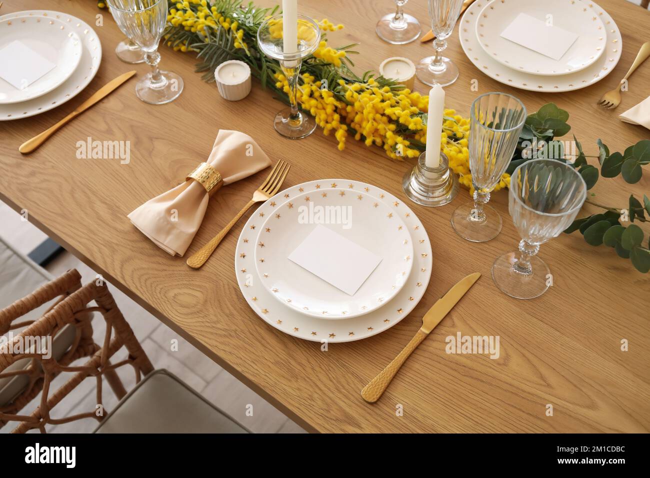 Beautiful table setting with mimosa flowers and candles in room Stock Photo