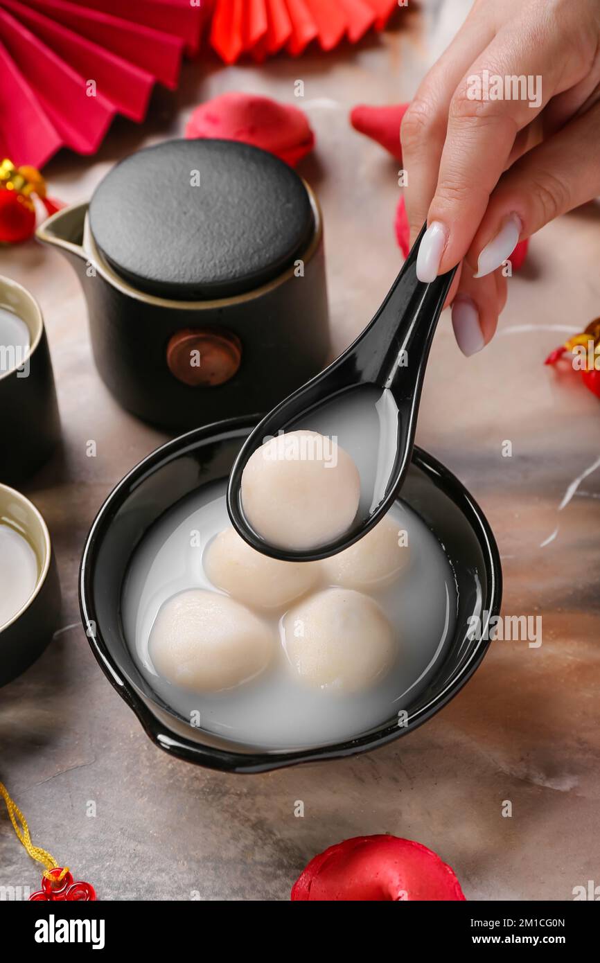 Woman with spoon and bowl of tangyuan on grunge background, closeup ...